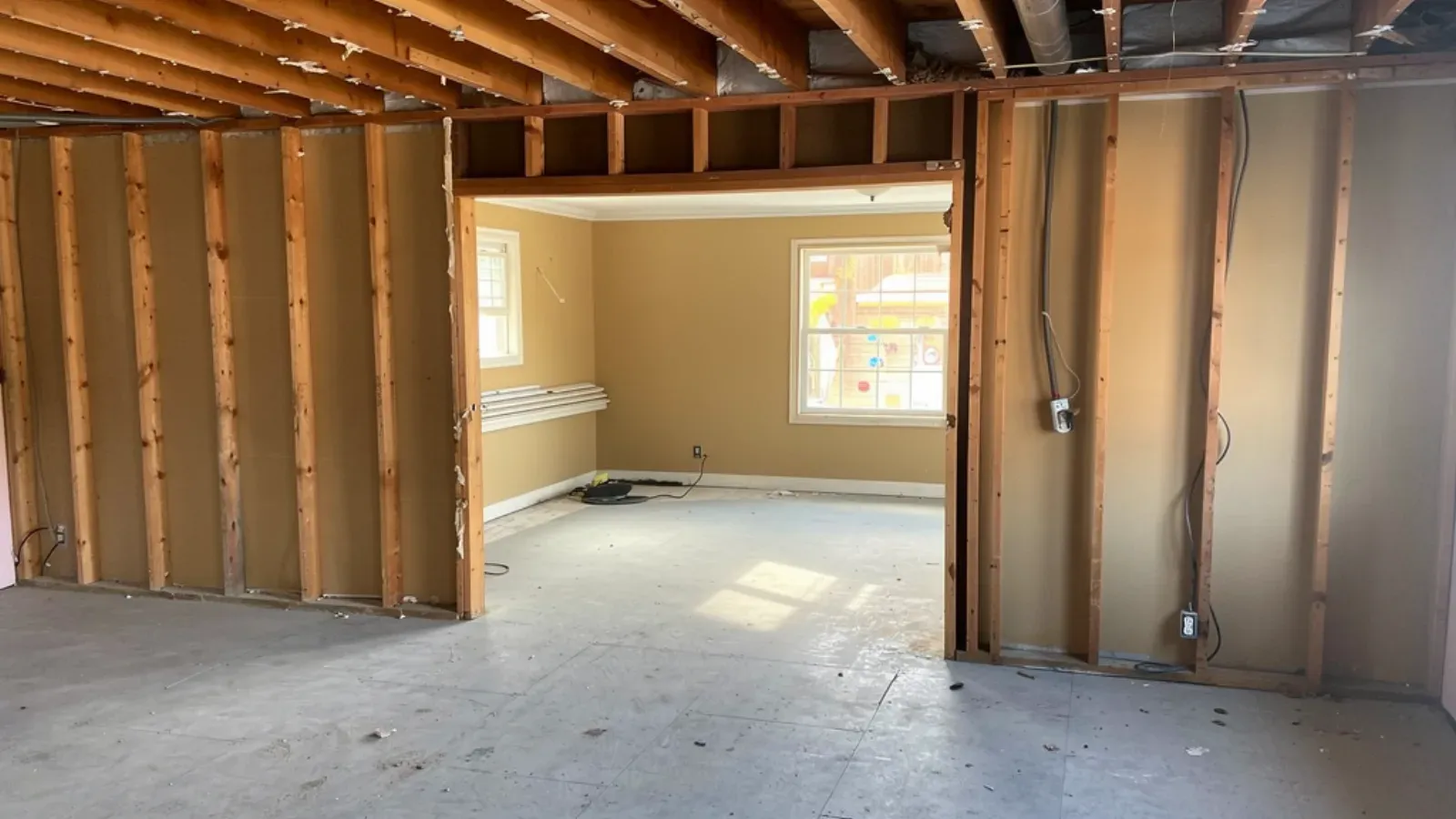 Interior room stripped to bare wood studs on two walls, ceiling joists exposed overhead and the floor swept clear