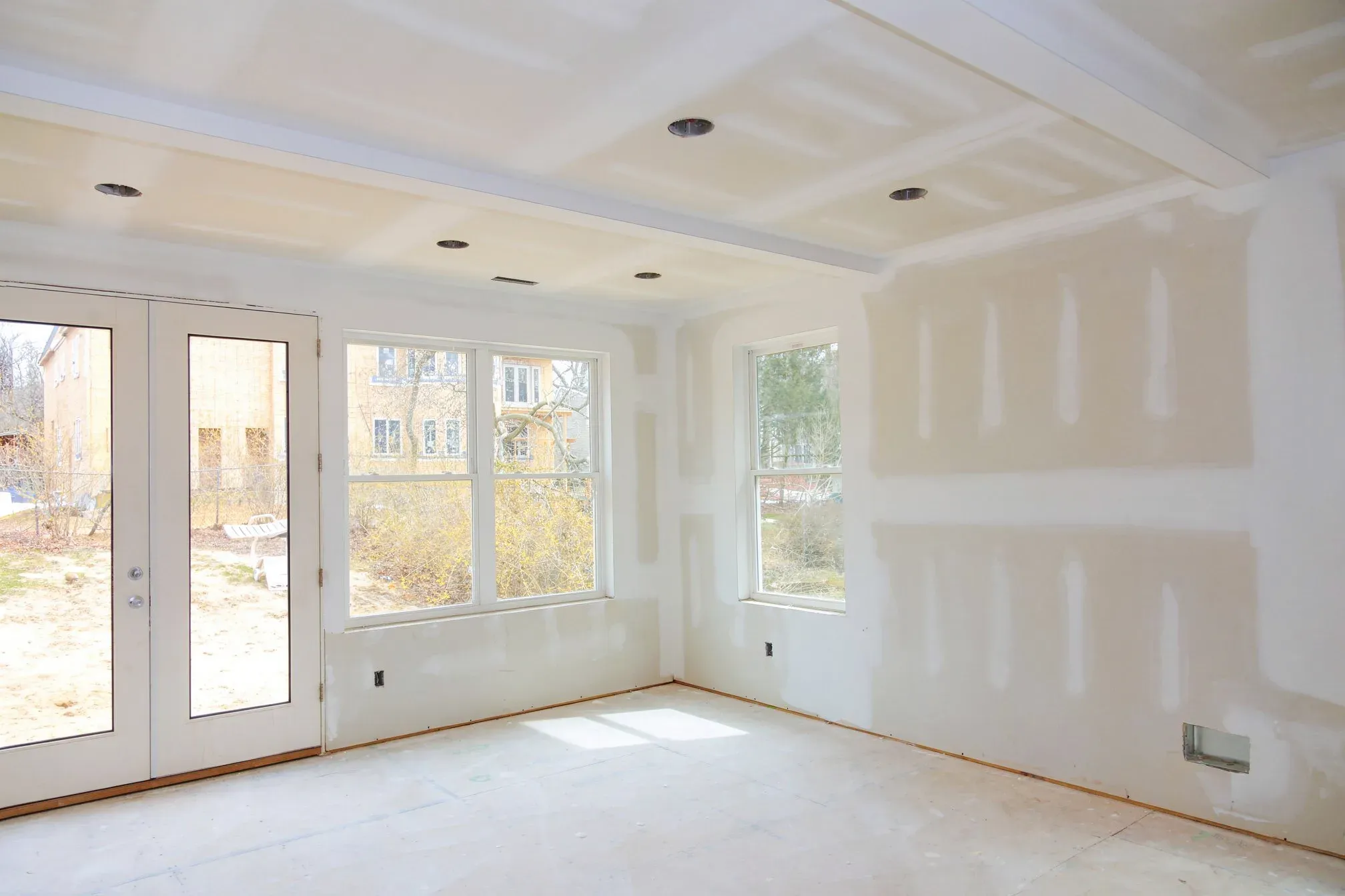 Interior room with newly hung and taped drywall, French doors and windows, awaiting finishing